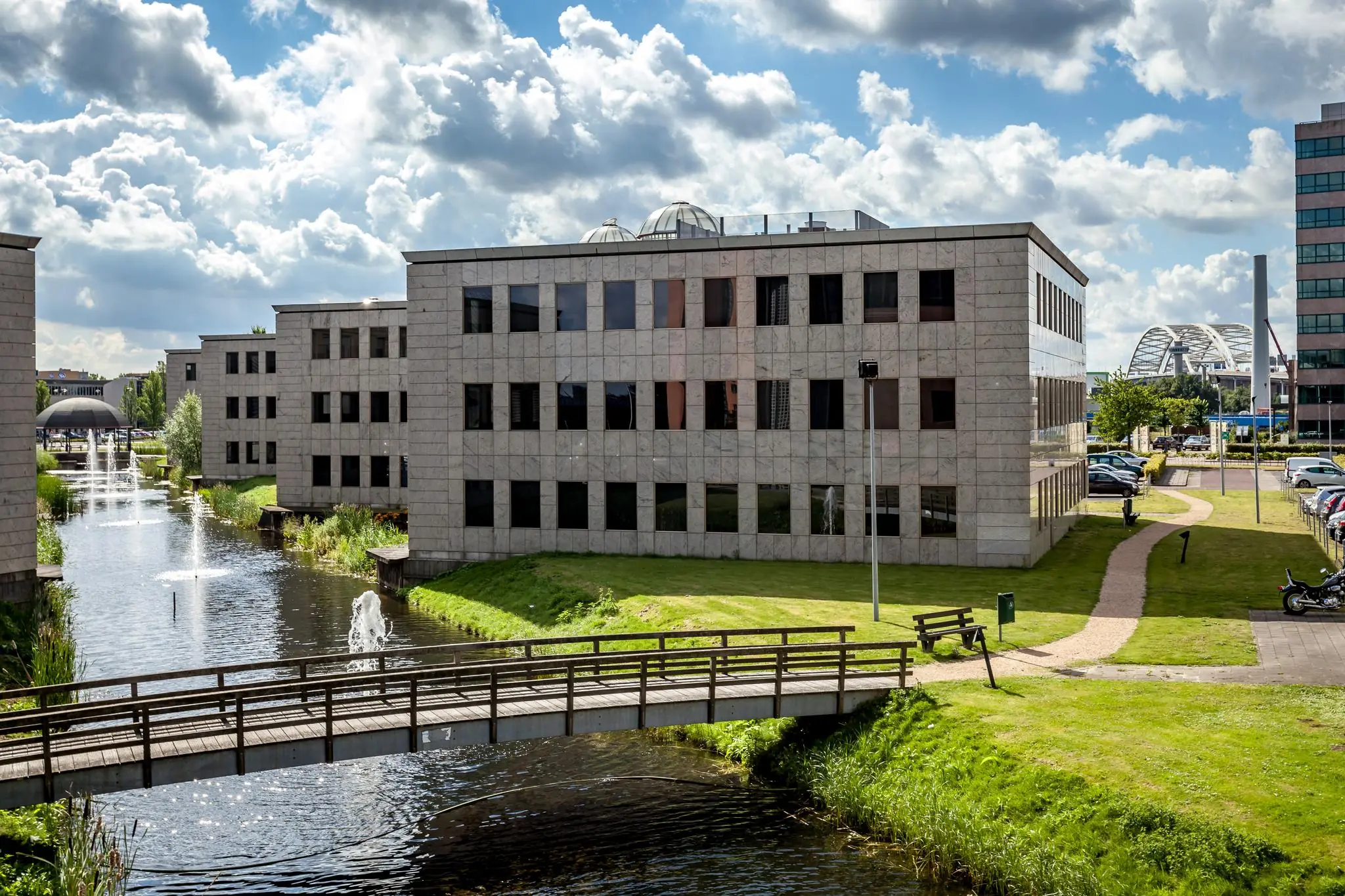 Kantoorgebouwen aan de Rivium 1e Straat met water, brug en fonteinen op de voorgrond.